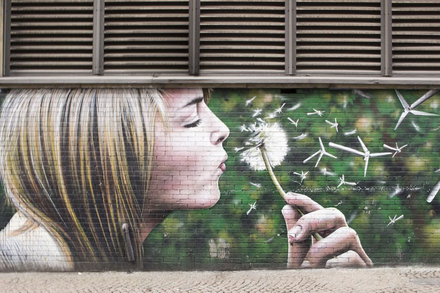 En väggmålning av en blond tjej som blåser en maskros på en vägg i Glasgow.
